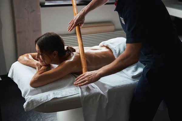 Mulher branca bonita sob a toalha relaxante e descansando enquanto recebendo terapia manual com massageador no centro de bem-estar — Fotografia de Stock