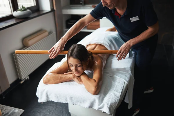 Entzückende hübsche Dame mit Handtuch entspannt sich bei der Massage manuelle Therapie mit Holzwerkzeug in der Klinik — Stockfoto
