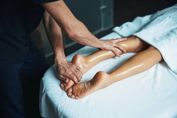 젊은 여성의 다리에 흰 수건을 두르고 미용 클리닉에서 남성의 손으로 신체 치료를 하는 모습 — 스톡 사진