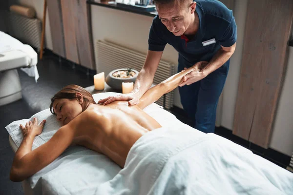 Mooie Kaukasische vrouw onder de handdoek ontspannen terwijl het krijgen van handmatige massage in spa salon — Stockfoto