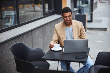 Ortağıyla sohbet eden esmer tenli bir adam.