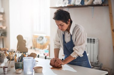 Attentive brunette woman kneading clay in pottery