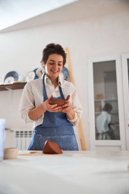 Young cute potter looking at piece of clay