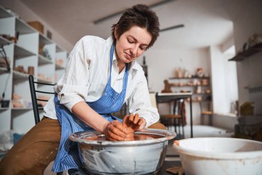Young attentive brunette creating clay vase in workshop