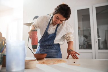 Young serious master looking at clay utensil