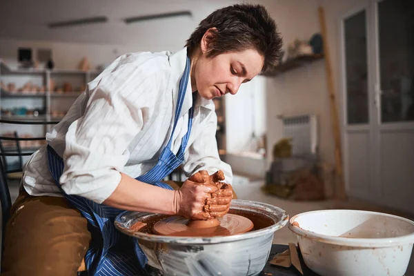 Concentrated woman sculpting clay pot on pottery wheel — Photo