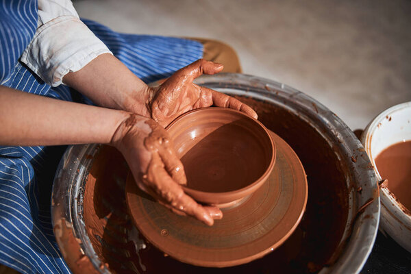 Female hands shaping clay pot on special wheel