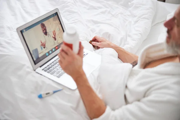 Бородатий чоловік дивиться на екран ноутбука, сидячи на ліжку в спальні — стокове фото
