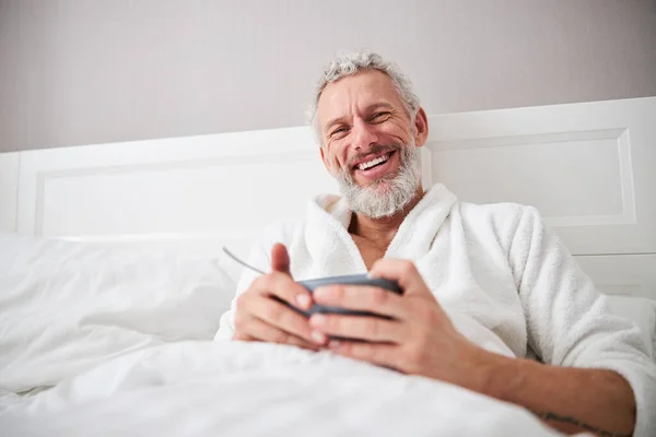 Bărbat adult cu barbă râzând bărbat odihnindu-se dimineața în apartament acasă — Fotografie, imagine de stoc
