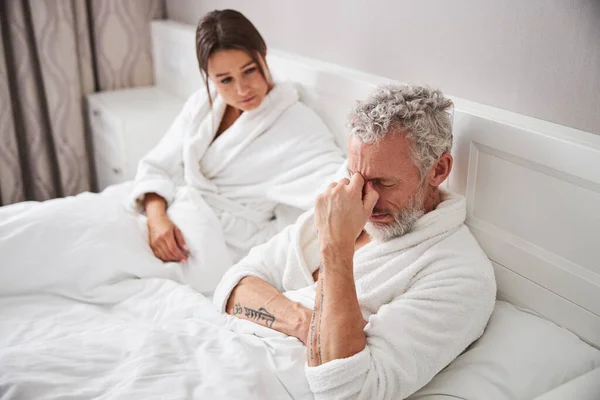 Thoughtful bearded man sitting on the bed with his wife in home apartment — Photo