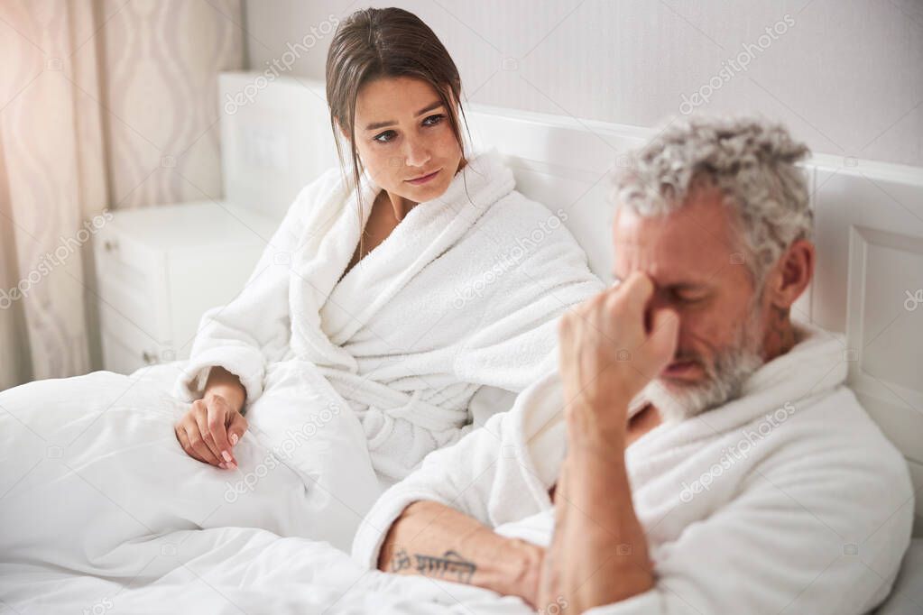 Beautiful Caucasian woman in white bathrobe taking care to her male in home apartment