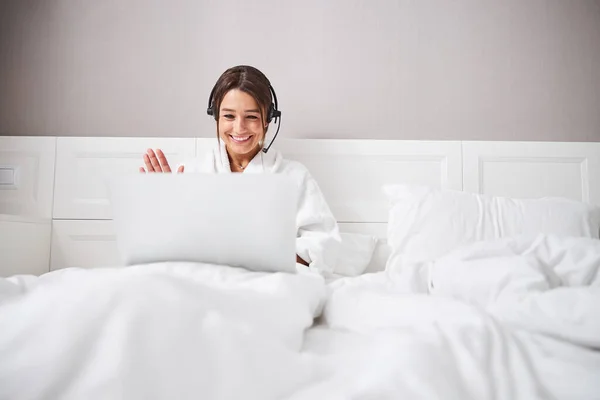 Hermosa joven con auriculares mirando a la pantalla de la computadora portátil en acogedor apartamento en casa — Foto de Stock