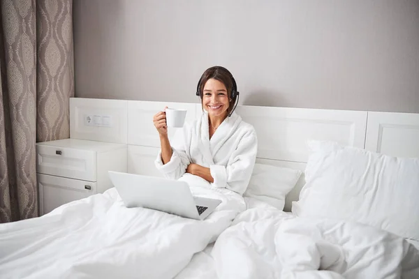 Attraktiv ung vit kvinna i hörlurar sitter vid laptop i sovrummet — Stockfoto