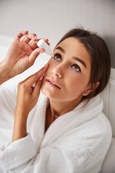 흰색 목욕 가운을 입은 아름다운 여인 이 집 아파트에서 눈 약을 먹고 있다 — 스톡 사진