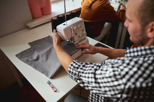 Male tailor sewing grey cloth with a machine — ストック写真