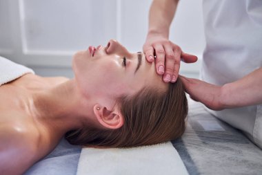 Calm elegant lady lying on the towel while getting professional skin care in spa resort hotel