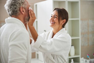 Young Caucasian beautiful female taking care to her husband while standing in room indoors
