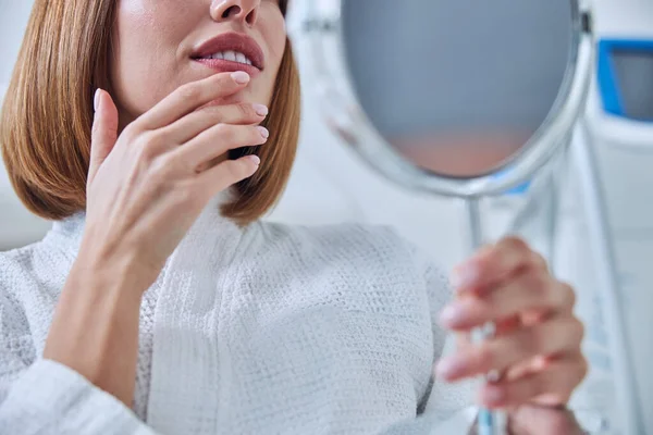Bájos fiatal hölgy tartja a kezét az arc közelében, miközben nézi a tükör a kozmetikai szekrény — Stock Fotó