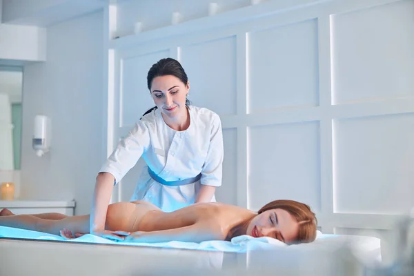 아름다운 붉은 머리 숙녀가 안마 침대에 누워 있는 동안 물리 치료사가 캐비닛 안에서 손을 마사지 한다 — 스톡 사진