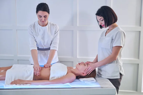 Professional beautician women in uniform making massage on body of young lady in spa center — ストック写真