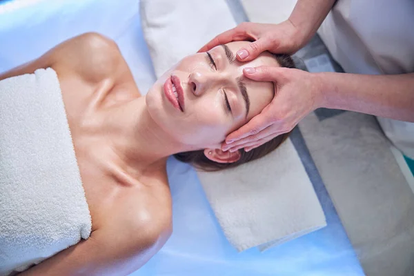 Beautiful elegant female with towel on her body relaxing at the spa face massage in spa salon — ストック写真