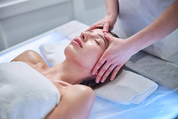 Mujer bastante caucásica tumbada en la mesa de masaje mientras disfruta del procedimiento de spa en el centro de spa — Foto de Stock