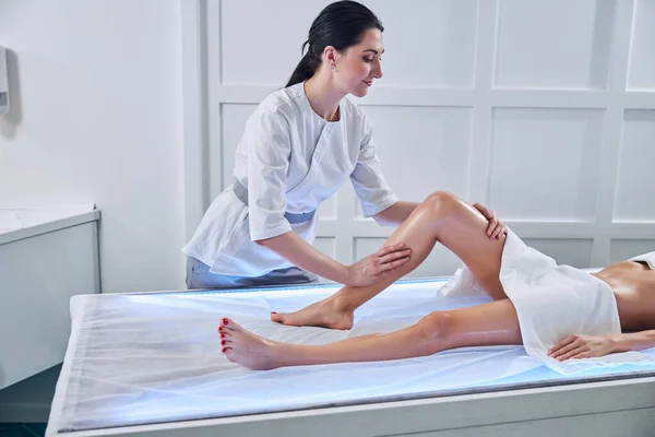 Szczęśliwy wesoły lekarz robi masaż antycellulitowy na stopach młodych kobiet — Zdjęcie stockowe
