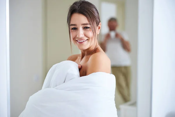 Sorridente bella femmina coperta di trapunta in piedi in camera bianca accogliente — Foto Stock