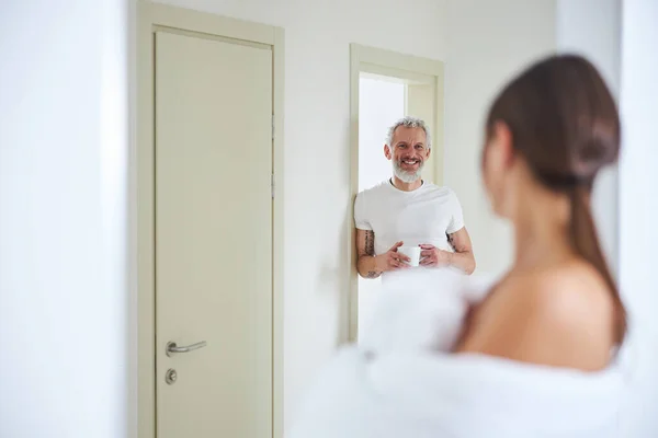 Homme adulte barbu avec tasse avec boisson à la main tout en restant debout dans l'appartement à la maison — Photo