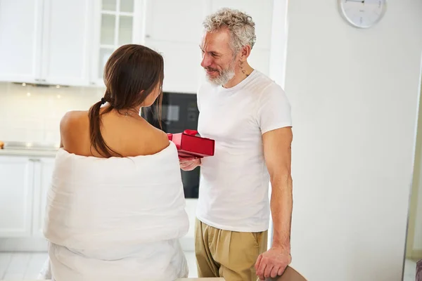 Brunette femelle debout devant son petit ami dans la couverture et de prendre un cadeau dans l'appartement à la maison — Photo