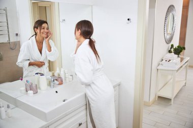 Pretty elegant Caucasian female taking face skin care in front of the mirror in room indoors