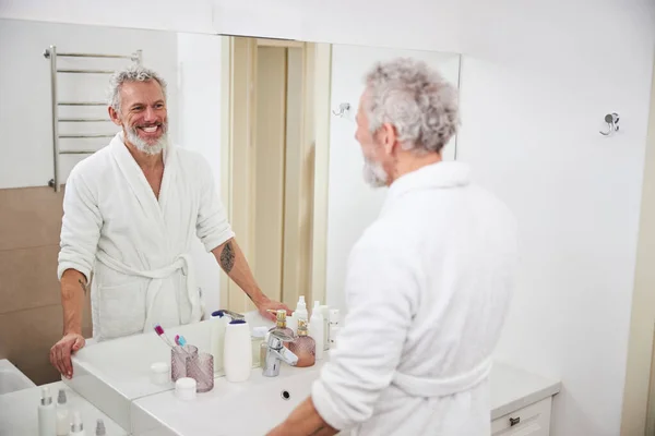 Felice maschio adulto sorridente guardando il riflesso nello specchio in bagno — Foto Stock