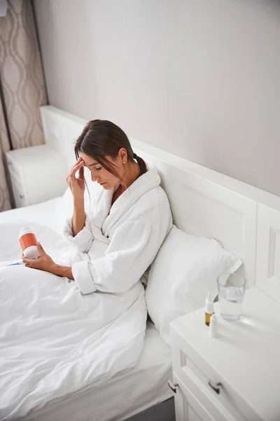 Hermosa mujer encantadora sensación de dolor de cabeza mientras está sentado en la cama en una habitación acogedora — Foto de Stock