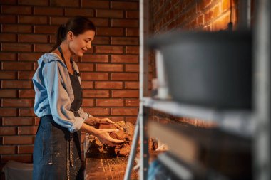 Mutlu gülümseyen beyaz kadın çömlek atölyesinde toprak malzemeleriyle şablon yapıyor.