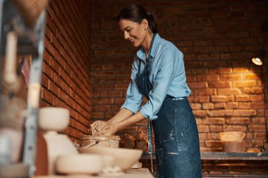 Önlük giyen zarif bayan sanatçı sanat stüdyosunda yeni ıslak toprak malzemeleriyle çalışıyor.