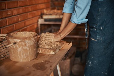 Önlüklü tanınmayan bir kadın sanat stüdyosunda toprak malzemeleriyle çalışıyor.