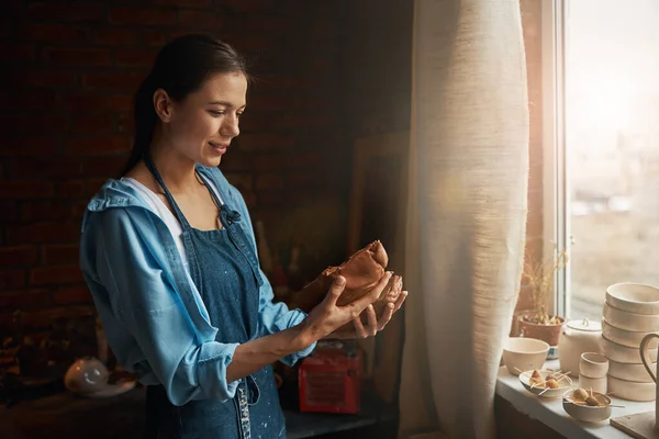 Frumoasă femeie sculptor ceramică care caută bucata de produs de pământ în brațe în atelier de ceramică — Fotografie, imagine de stoc
