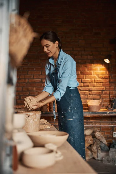 Szczęśliwy wesoły brunetka kobieta wyciskając kawałki materiałów ceramicznych nad wiadro w warsztacie ceramiki — Zdjęcie stockowe
