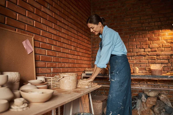 Jonge blanke ambachtelijke vrouw opknoping in kunst studio terwijl knijpen aardewerk materialen in kunst studio — Stockfoto