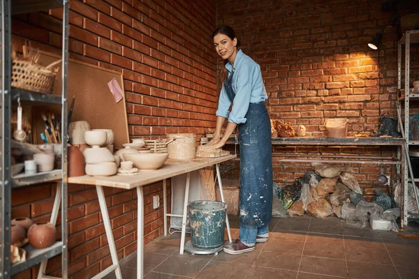 Hermosa elegante mujer artesana caucásica usando delantal exprimiendo arcilla en taller de cerámica —  Fotos de Stock