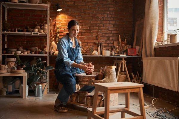 Encantadora artesana caucásica con delantal haciendo algo en la rueda de cerámica en el taller —  Fotos de Stock