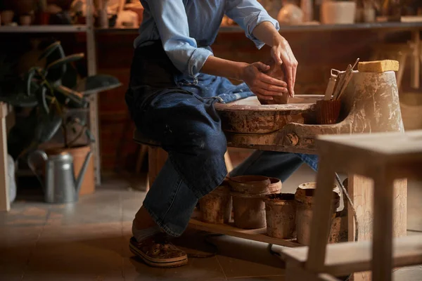 Красива невідома ручна ремесла жінка в фартусі, що сидить в художній студії, моделюючи щось з глини — стокове фото
