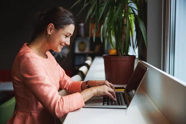 Charmig kaukasisk kvinnlig affärsanalytiker skriva något på nätbok medan du sitter vid skrivbordet — Stockfoto