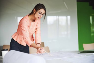 Young Caucasian female designer working with drawings on the work table in the modern bright office