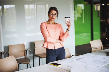 Charming successful female business analyst in formal wear and glasses standing near the work desk