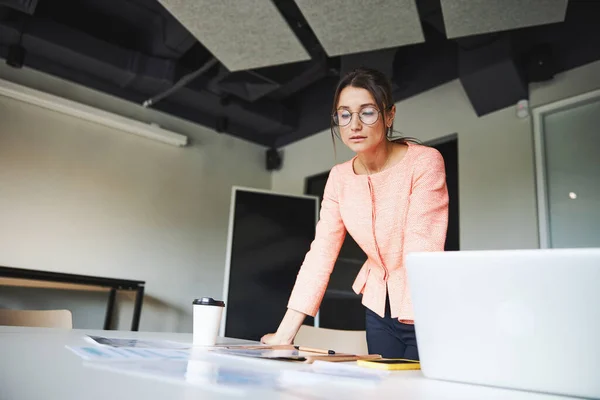 Young cheerful Caucasian female business consultant looking through the report on the table — 스톡 사진