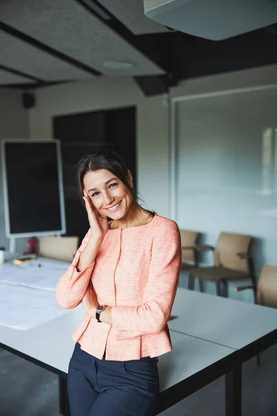 Charming brunette woman business analyst in pink jacket leaning on the work desk in the meeting room — Stockfoto