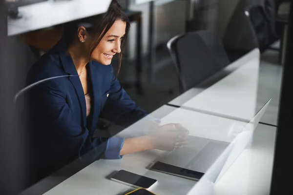 Gorgeous business lady wearing dark blue jacket looking to the screen of laptop in room indoors — ストック写真