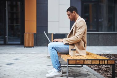 Koyu tenli dikkatli bir adam dizüstü bilgisayarına bakıyor.