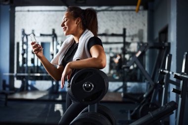 Spor salonunda akıllı telefonuyla gülümseyen bayan spor eğitmeni.